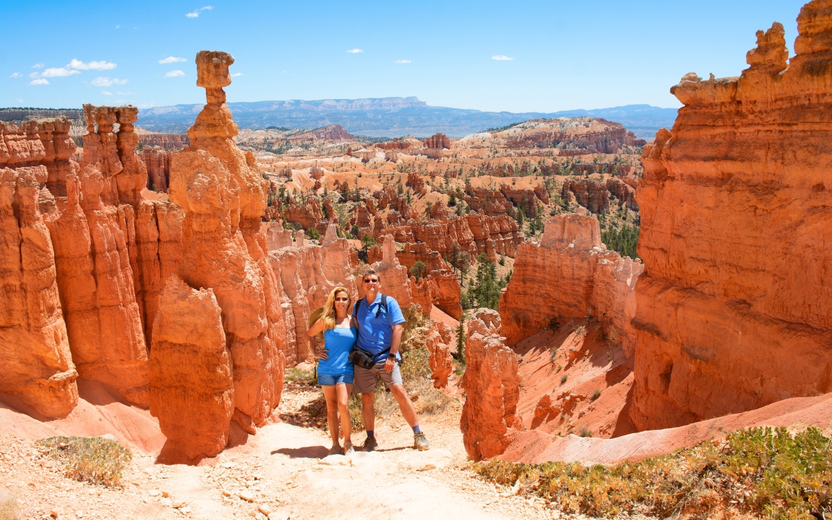 People enjoying summer hiking trip standing next to famous Thor's Hammer hoodoo. Smiling happy couple embracing on vacation in the red mountains. Bryce Canyon National Park, Utah, USA